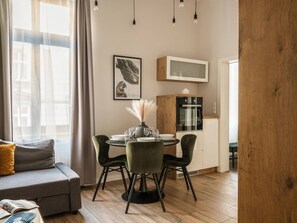 A modern living room with a gray sofa, a dining table with four chairs, and a kitchen area with a microwave and cabinets. - Green Boho 2-bed family apt in the city center (Kraków)