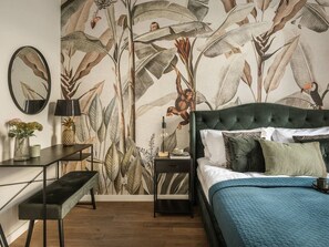 A bedroom with a large bed, a desk, a chair, a nightstand, and a wall with a nature-themed mural. - Green Boho 2-bed family apt in the city center (Kraków)