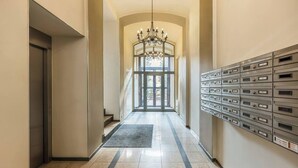 Un corridoio con un lampadario, cassette delle poste e una porta che dà su una stanza luminosa.
