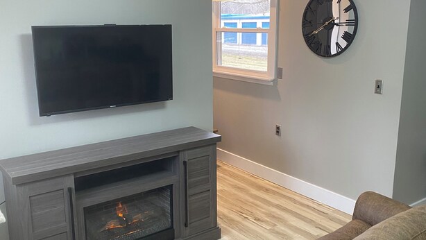 Una sala de estar con un televisor de pantalla plana montado en la pared, una chimenea de madera oscura y un sofá de cuero marrón.