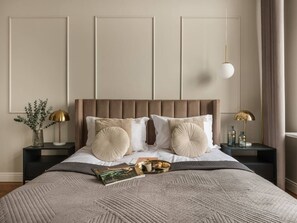 Una cama bien tendida con un cabecero, dos mesitas de noche con lámparas y una revista sobre la cama.
