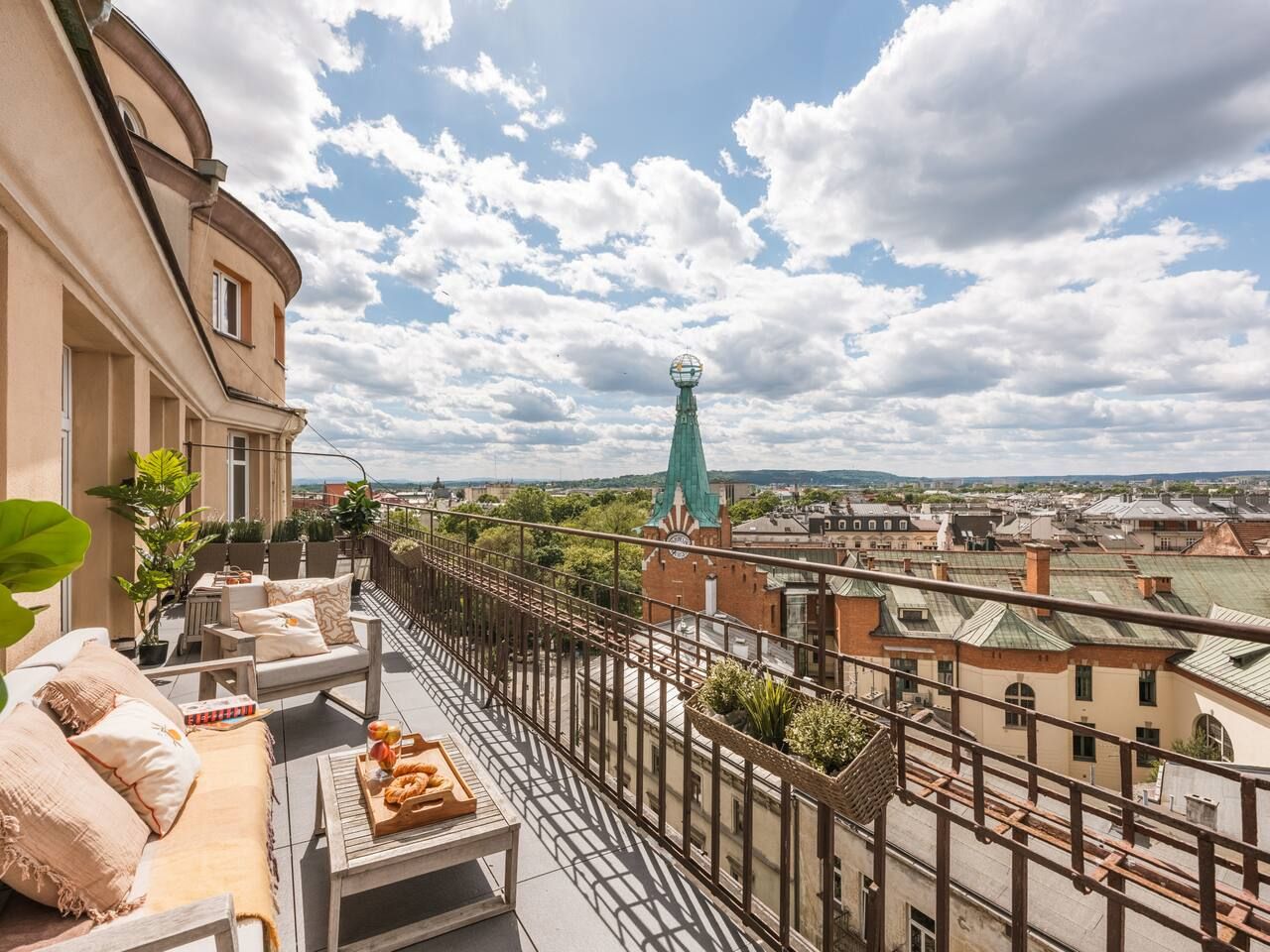 Un balcon avec des sièges d’extérieur, une vue sur le paysage urbain et une tour verte remarquable qui se distingue à l’horizon.