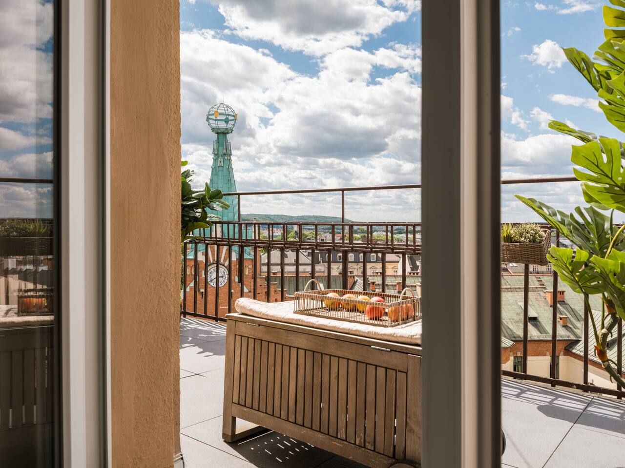 Een dakterras met uitzicht op een toren, een houten bankje en een metalen hekwerk.