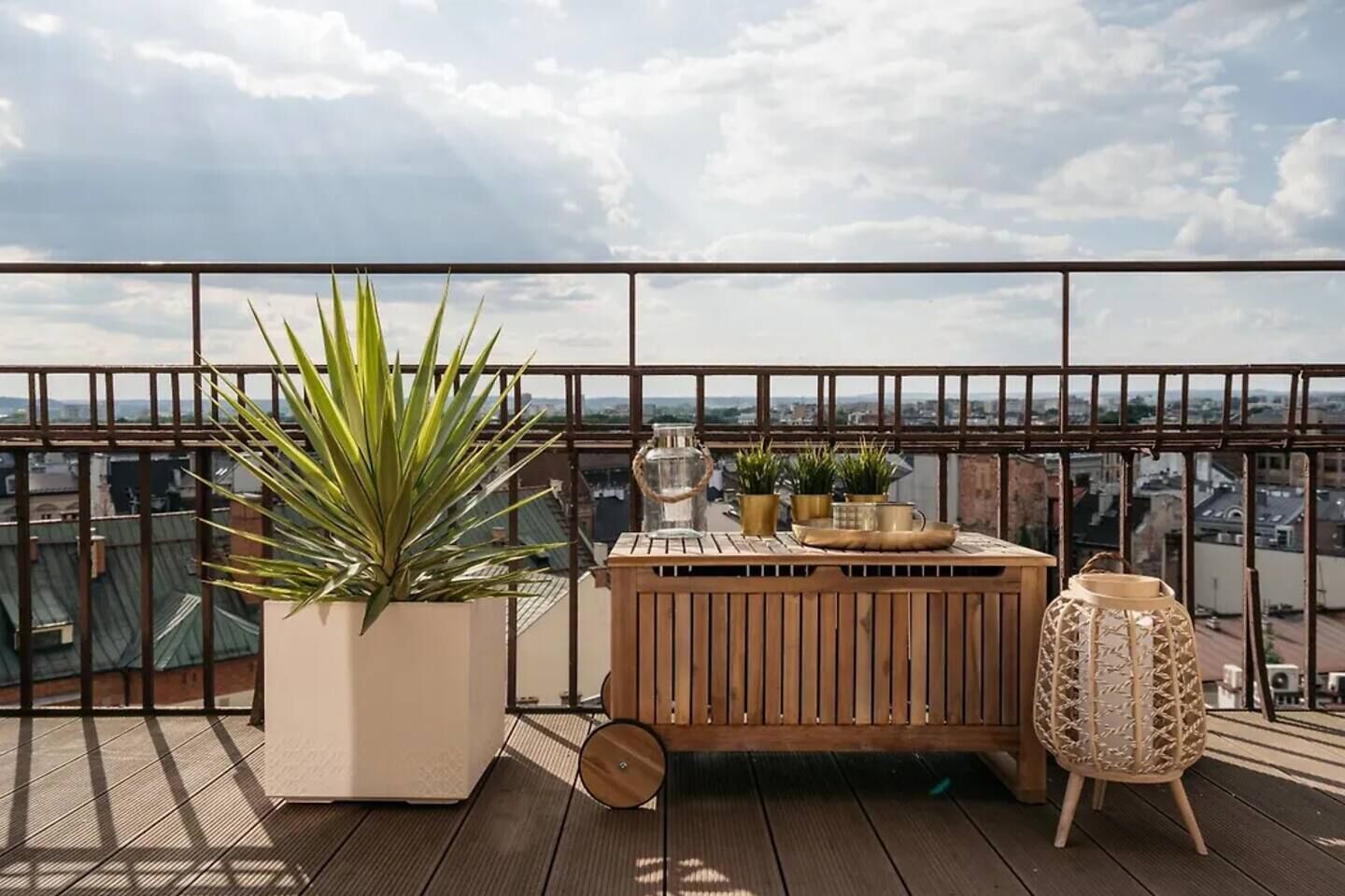 Un balcon agrémenté d’un pot de fleurs, une table en bois décorée de divers objets, et une chaise en osier.