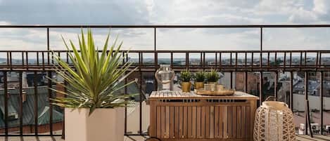 A balcony with a potted plant, a wooden table with decorative items, and a wicker chair.