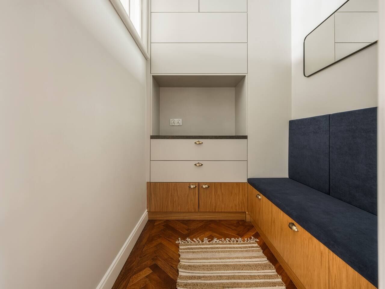 A narrow hallway with a bench, wooden cabinets, and a mirror on the wall.
