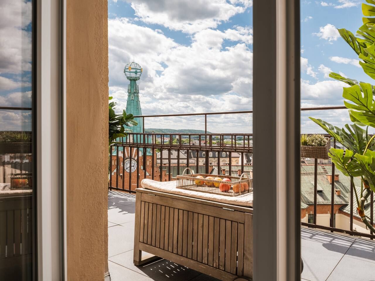 Un balcon donnant sur une tour, un banc en bois et une rambarde en métal.