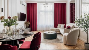 A modern living room with a dining area, red curtains, a sofa, and a potted plant. - 3-bedroom apartment Merlot (Kraków)