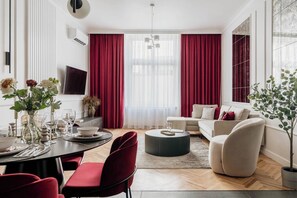 A modern living room with a dining area, red curtains, a sofa, and a potted plant. - 3-bedroom apartment Merlot (Kraków)