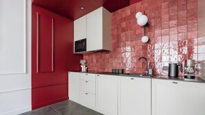 A modern kitchen with white cabinets, a red backsplash, and a black coffee machine. - 3-bedroom apartment Merlot (Kraków)