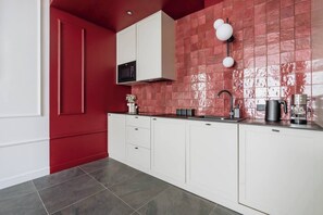 A modern kitchen with white cabinets, a red backsplash, and a black coffee machine. - 3-bedroom apartment Merlot (Kraków)