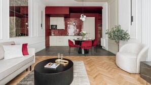 A modern living room with a sofa, a dining table with chairs, a coffee table, and a potted plant. - 3-bedroom apartment Merlot (Kraków)