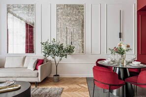 Un salon moderne avec un canapé, une table à manger pour quatre personnes et une grande fenêtre agrémentée de rideaux.