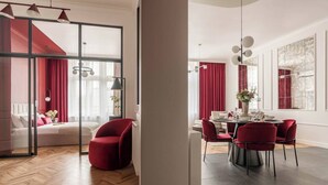 A modern hotel room with a large bed, a dining area with a table set for four, and a red chair. - 3-bedroom apartment Merlot (Kraków)