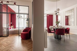 A modern hotel room with a large bed, a dining area with a table set for four, and a red chair. - 3-bedroom apartment Merlot (Kraków)