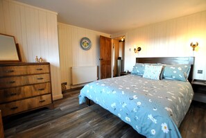 A bedroom with a wooden dresser, a bed with floral bedding, a radiator, and a door leading to another room. - Sma' Gift- Seafront sanctuary in ST Monans (Saint Monans)