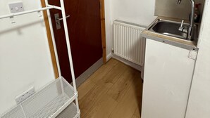 A compact room with a wooden door, a white radiator, a sink, and metal shelves. - Double Bedroom with Attached Bathroom in Blackpool-Families and Couplies Only (Blackpool)