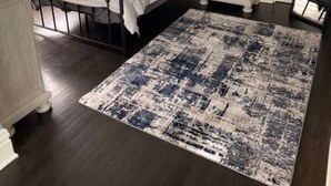 A bedroom with a bed, bedside table, lamp, and a large rug.