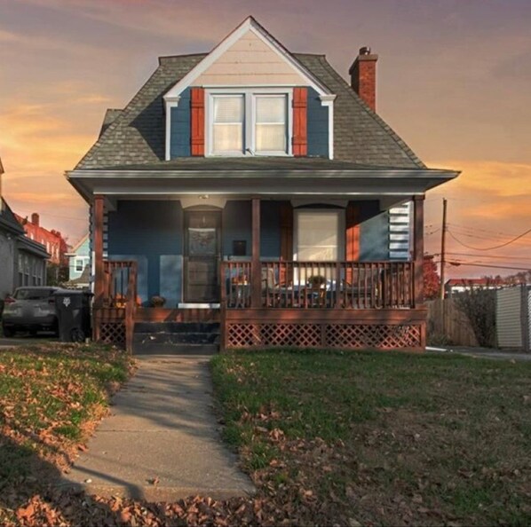A two-story house with a front porch, a chimney, and a pathway leading to the entrance.