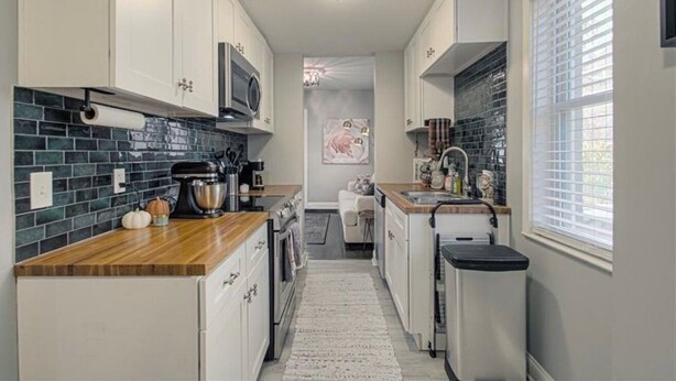 A narrow kitchen with white cabinets, a wooden countertop, a microwave, and a coffee maker.