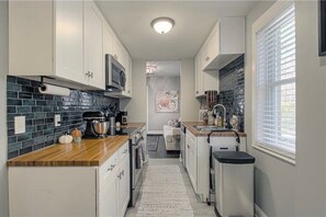 A narrow kitchen with white cabinets, a wooden countertop, a microwave, and a coffee maker.