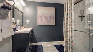 A modern bathroom with a dark gray wall, a white sink, a large mirror, and a shower with a glass door.