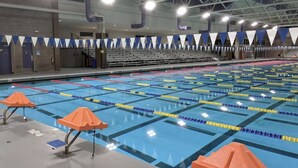 Una piscina con divisiones para carriles, sillas de salvavidas anaranjadas y un techo alto con vigas estructurales visibles.