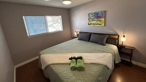 Un dormitorio con cama, ventilador de techo, ventana y un cuadro colgado en la pared.