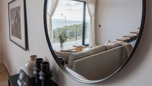 En moderne stue med et stort spejl, der viser udsigt til en balkon, en sofa, et lille bord og et billede i ramme på væggen.
