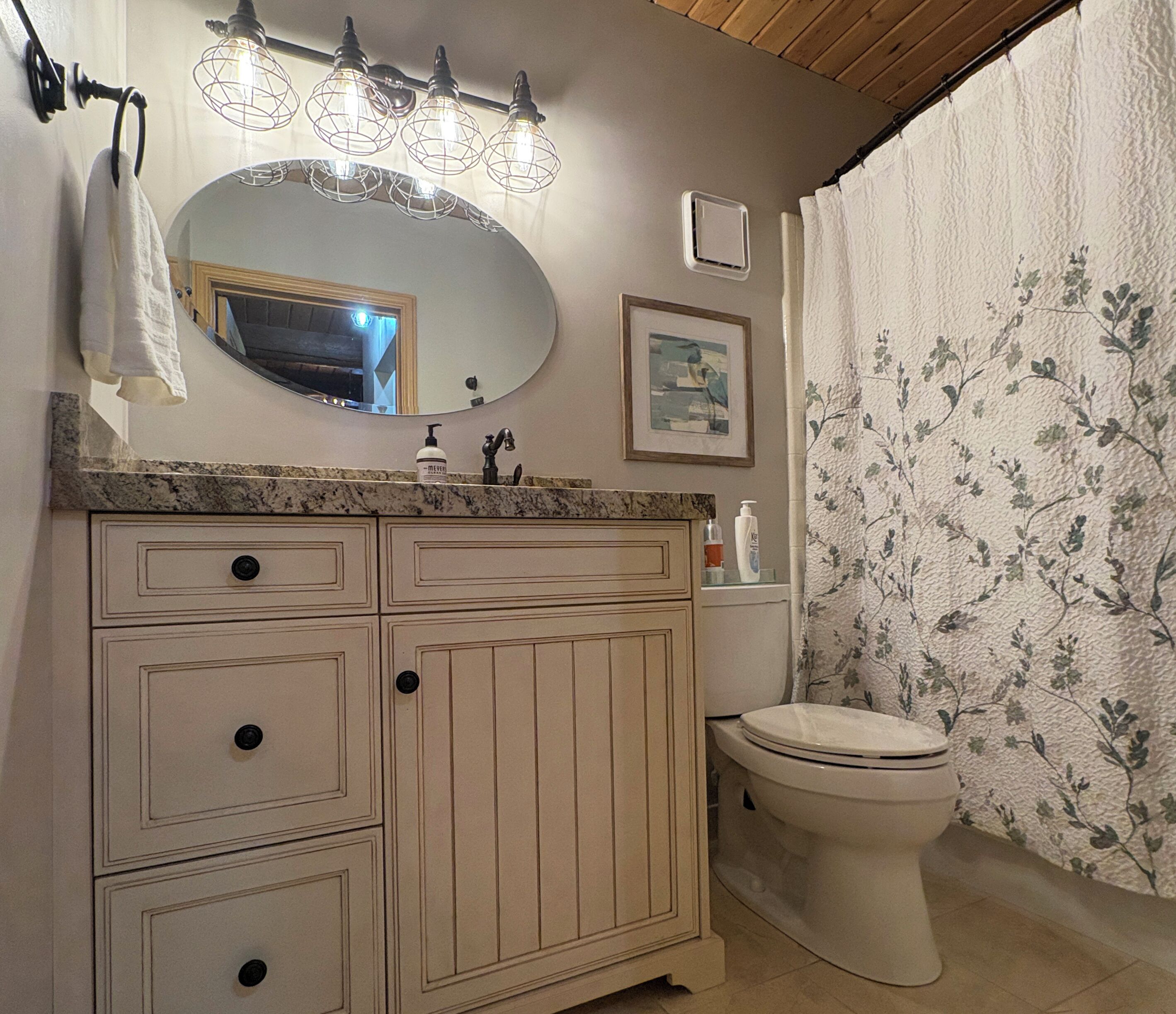 Une salle de bain avec un comptoir en marbre, un lavabo, des toilettes, un miroir et un rideau de douche orné d’un motif floral.