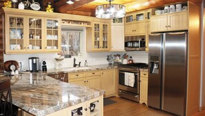 A kitchen with wooden cabinets, granite countertops, stainless steel appliances, and a hanging light fixture.