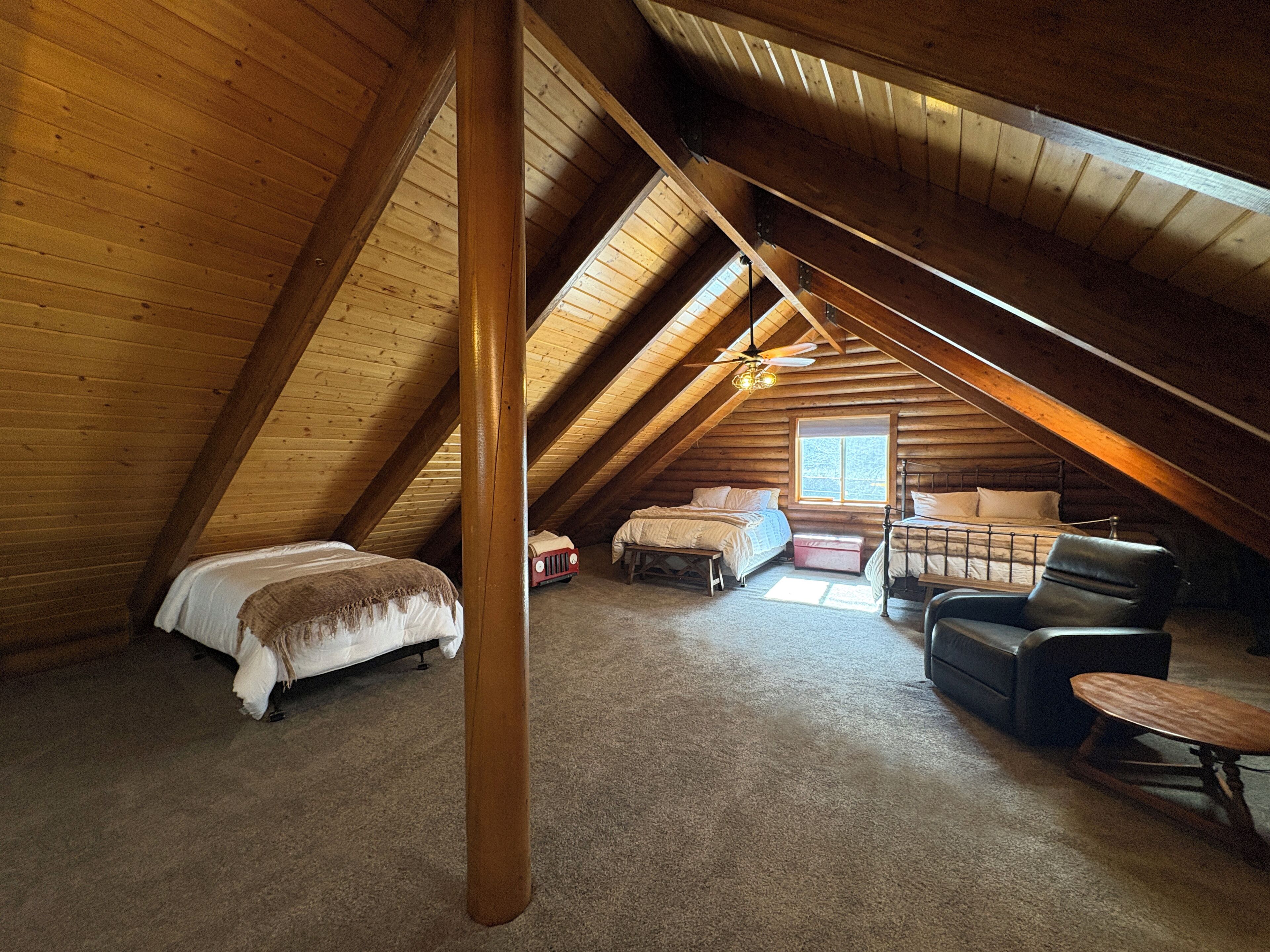 A cozy attic bedroom with a sloped ceiling, wooden beams, a bed, a chair, and a small table.