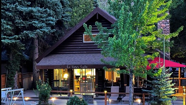 A log cabin with a porch, outdoor seating, and a stone wall.
