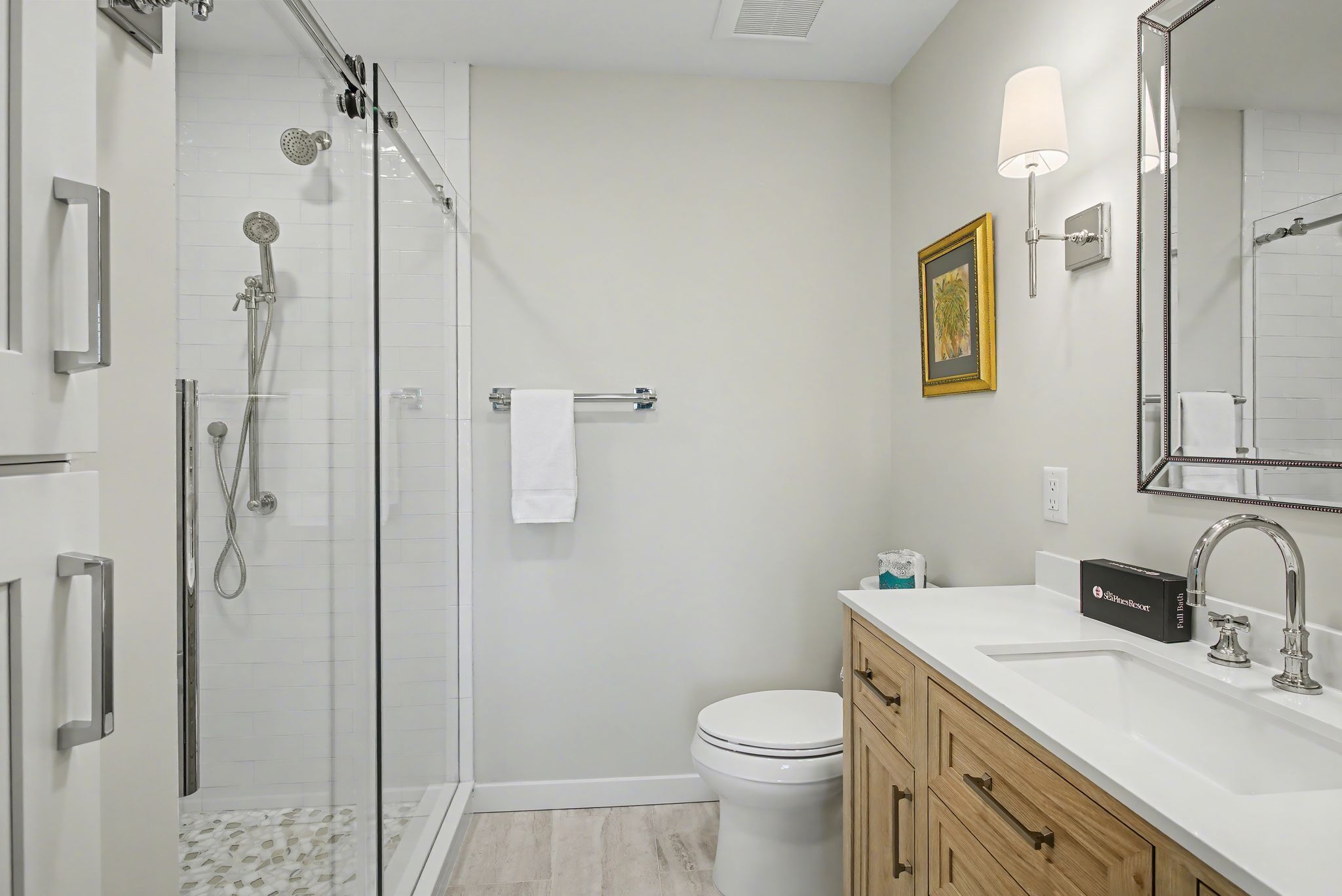 A modern bathroom with a glass-enclosed shower, a toilet, a sink with a mirror, and a towel rack.