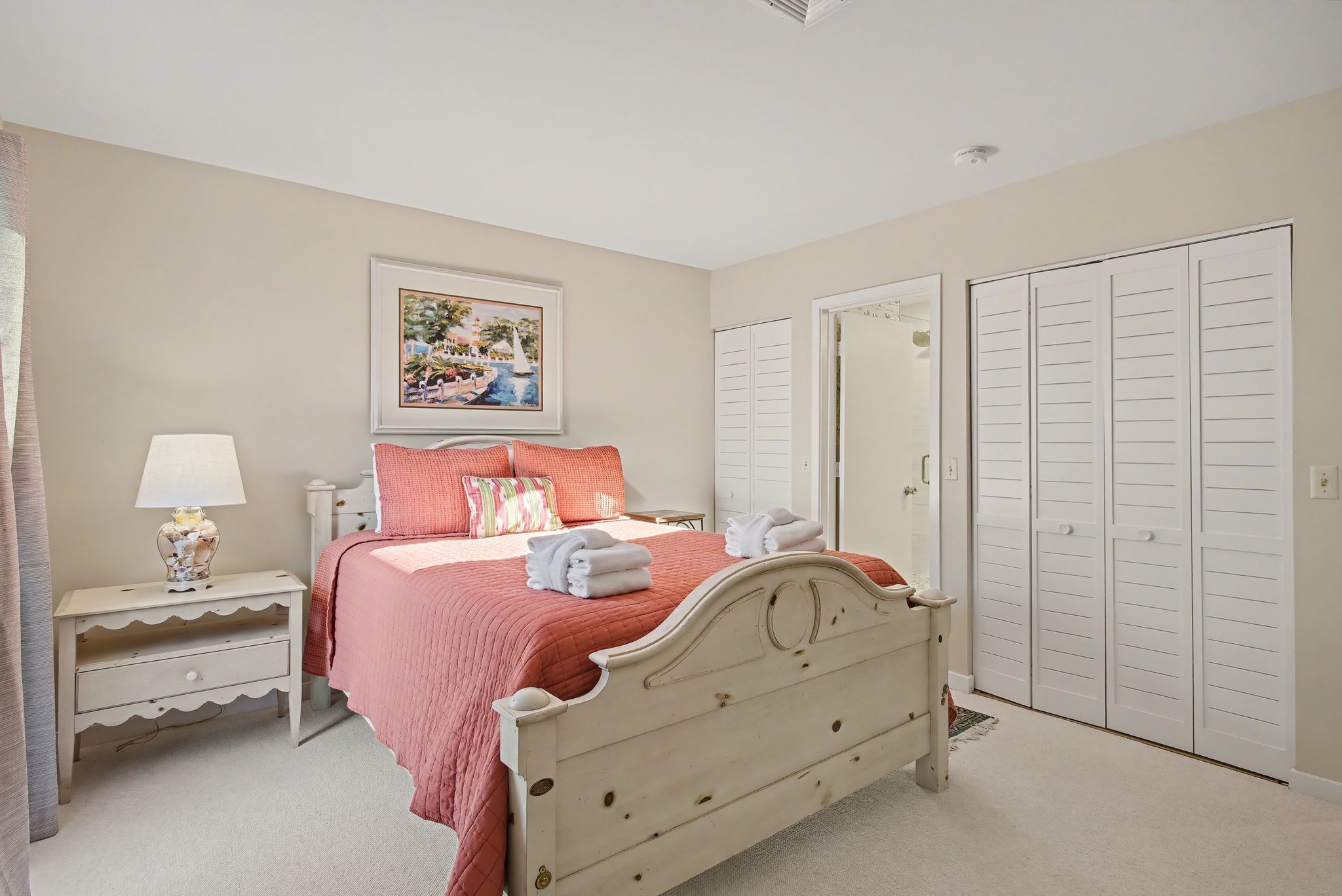 A bedroom with a bed, a nightstand, a lamp, a painting, and a wardrobe.