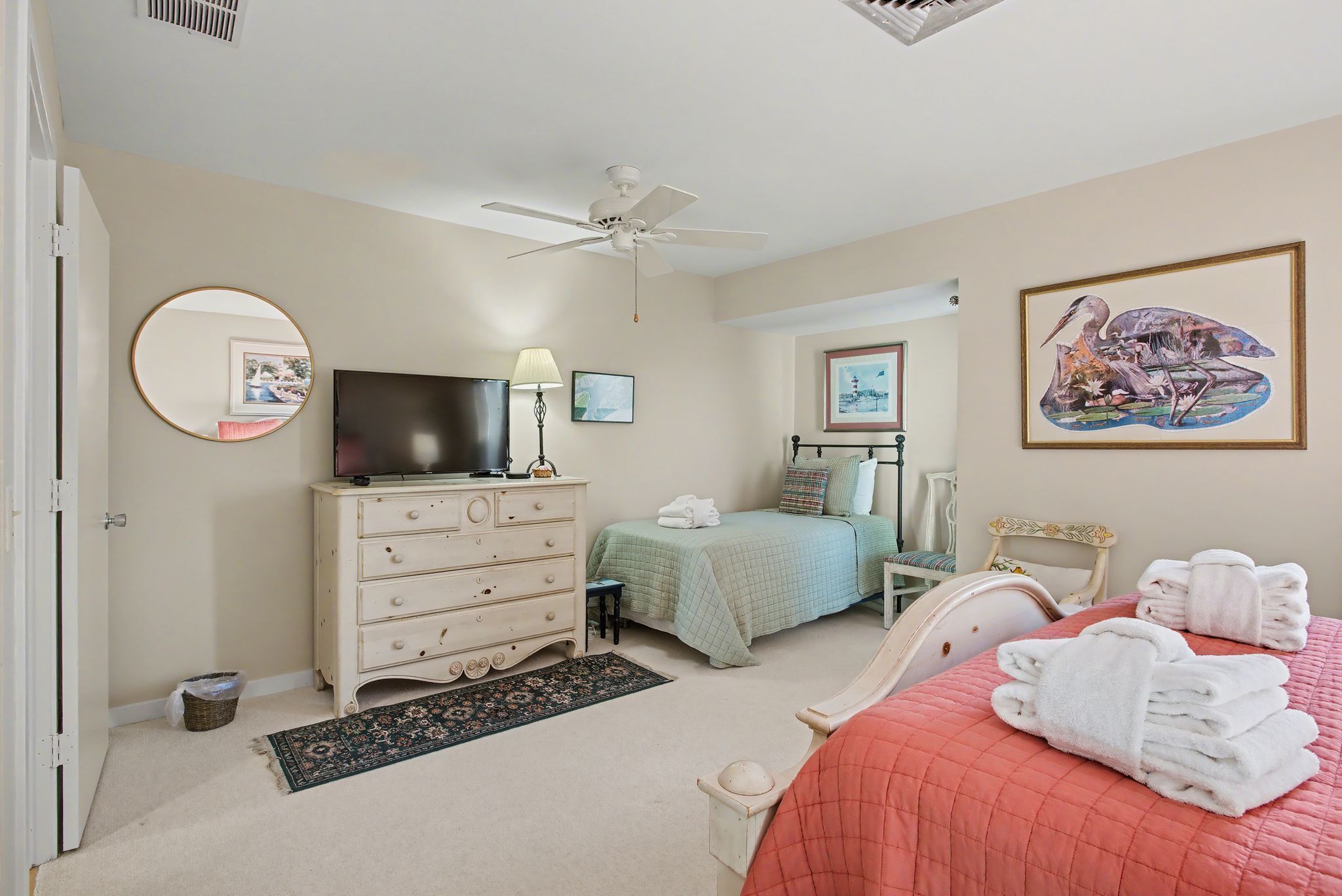 A bedroom with a bed, a dresser, a television, a ceiling fan, and artwork on the walls.