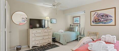 A bedroom with a bed, a dresser, a television, a ceiling fan, and artwork on the walls.