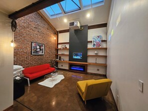 A living room with a red sofa, a yellow armchair, a TV, and a brick wall.