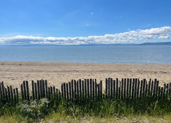 A beach with a wooden fence in the foreground and a calm sea in the background.