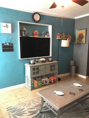 A living room with teal walls, a large flat-screen TV, a coffee table, and a small table with a basket.