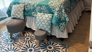 Une chambre avec une couvre-lit à motifs floraux aux tons turquoise et blanc, une croix au mur, un autocollant représentant un arbre et un tapis à motifs.