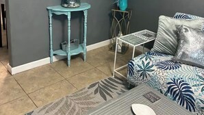 Un salon avec un mur gris, un miroir doté d’un cadre bleu, un canapé bleu agrémenté de coussins à motifs, une petite table sur laquelle est posé un vase, et un tapis orné de motifs de feuilles.