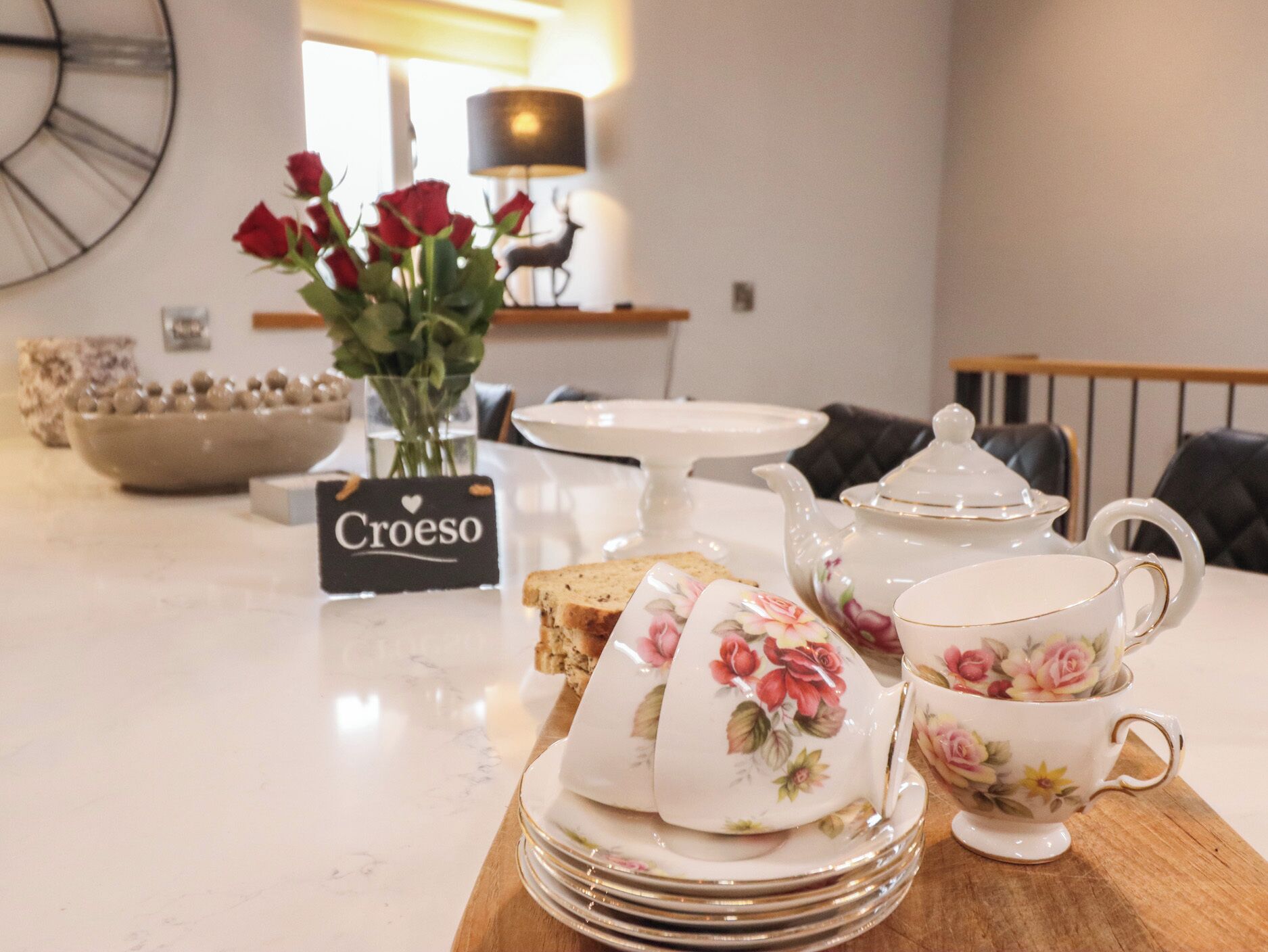 Una mesa de comedor con una tetera floral, tazas y un cartel que dice 'Croeso'.