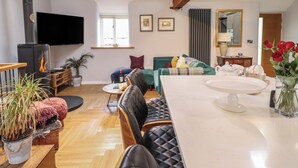 A cozy living room with a fireplace, a sofa, a dining table, and a TV mounted on the wall. - The Old Cartshed Yr Hen Gwt Cart (Abergele)
