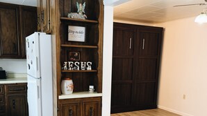A kitchen with wooden cabinets, a white refrigerator, and a decorative shelf with items. - Cozy 2-Bedroom Hulett Home Near Devils Tower & Black Hills (Hulett)