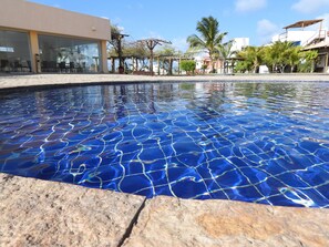 Ein klares Schwimmbecken mit einer gefliesten Kante, umgeben von einem Gebäude mit großen Fenstern und Außenmöbeln.