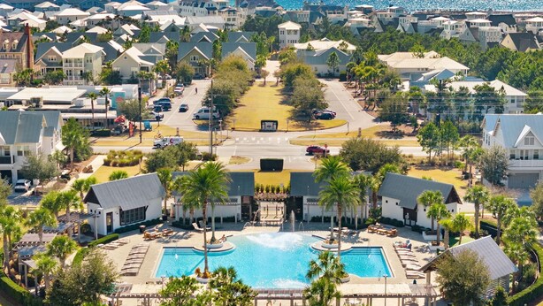 Vista aérea de una zona residencial costera con una piscina central rodeada de palmeras y sillones de descanso.