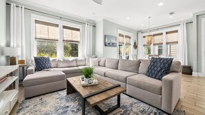 Una sala moderna con un sofá modular, una mesa de centro de madera y ventanas grandes con persianas.