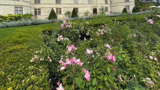 Un grand bâtiment historique doté de nombreuses tours et d’un jardin bien entretenu où poussent des fleurs roses.