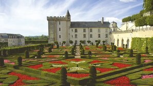 Un grand bâtiment historique doté d’un jardin à la disposition symétrique, agrémenté de haies taillées et de parterres de fleurs.